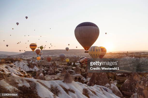hot air balloons flying over rocky landscape against clear sky in goreme during sunset, cappadocia, turkey - cappadocia hot air balloon stock pictures, royalty-free photos & images