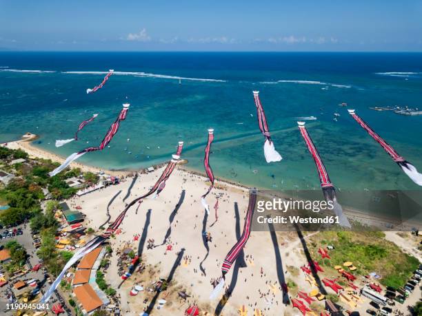 drone shot of kites flying over beach against blue sky during festival, bali, indonesia - indonesian kite stock pictures, royalty-free photos & images