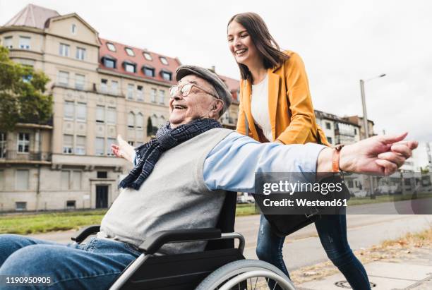 laughing young woman pushing happy senior man in wheelchair - alter mann jung geblieben stock-fotos und bilder