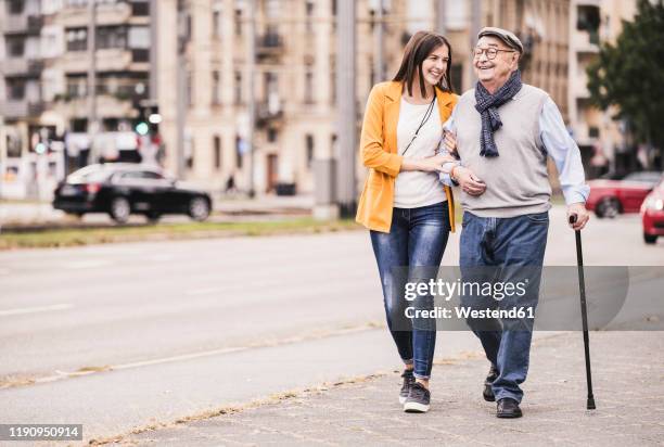 adult granddaughter assisting her grandfather strolling with walking stick - pedestrian walkway stock-fotos und bilder