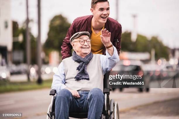 portrait of laughing young man pushing happy senior man in wheelchair - rollstuhl schieben stock-fotos und bilder