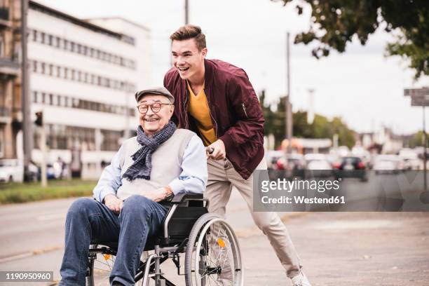 laughing young man pushing happy senior man in wheelchair - support stock-fotos und bilder