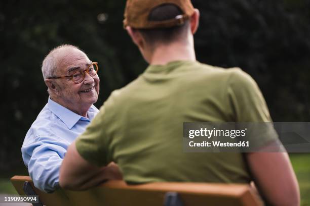 portrait of smiling senior man relaxing together with his grandson on a park bench - doing a favor stockfoto's en -beelden