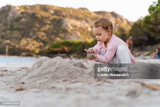 cute toddler girl playing with sand on the beach - kind sandburg stock-fotos und bilder
