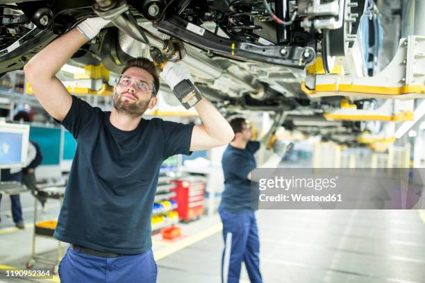 two colleagues working at car underbody in modern factory - car factory stock-fotos und bilder