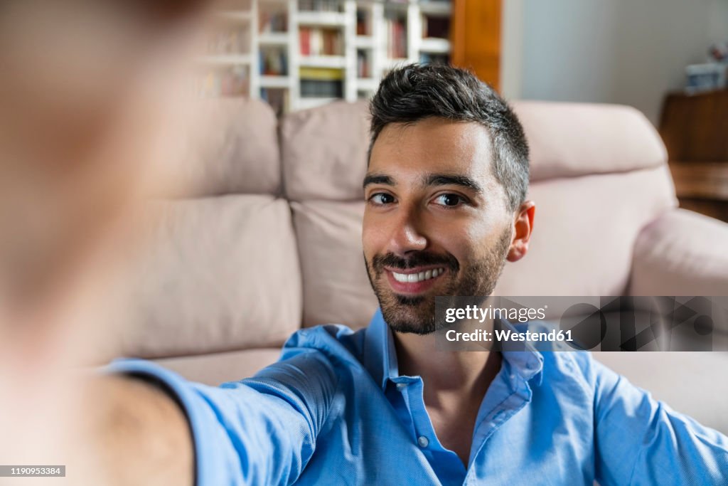 Portrait of smiling young man taking selfie at home