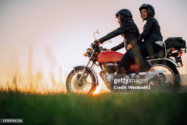 young couple on vintage motorbike at sunset - vintage motorcycle helmet stock pictures, royalty-free photos & images