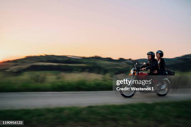 young couple riding vintage motorbike on country road at sunset, tuscany, italy - driving romance stock-fotos und bilder