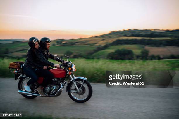 young couple riding vintage motorbike on country road at sunset, tuscany, italy - motociclista foto e immagini stock
