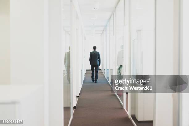 rear view of businessman walking down office corridor - arbeitslosigkeit stock-fotos und bilder