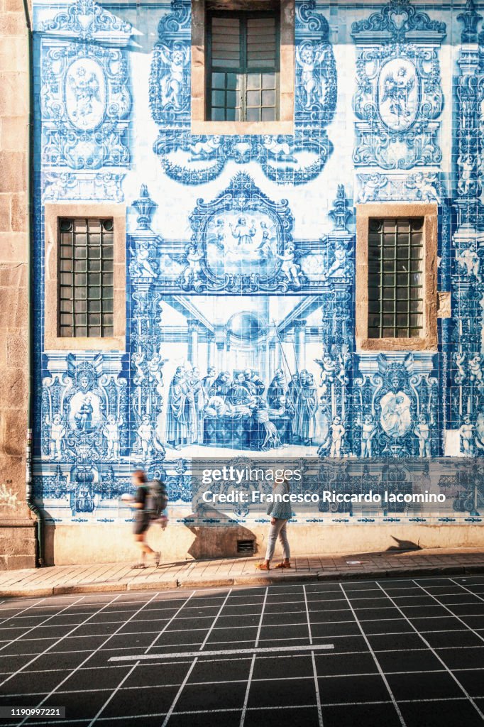Woman walking in Porto against azulejos wall of the Capela das Almas church in Porto