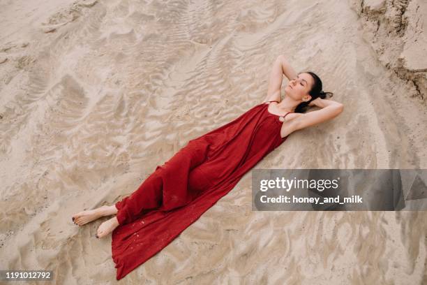 woman lying in the sand daydreaming, russia - red dress ストックフォトと画像