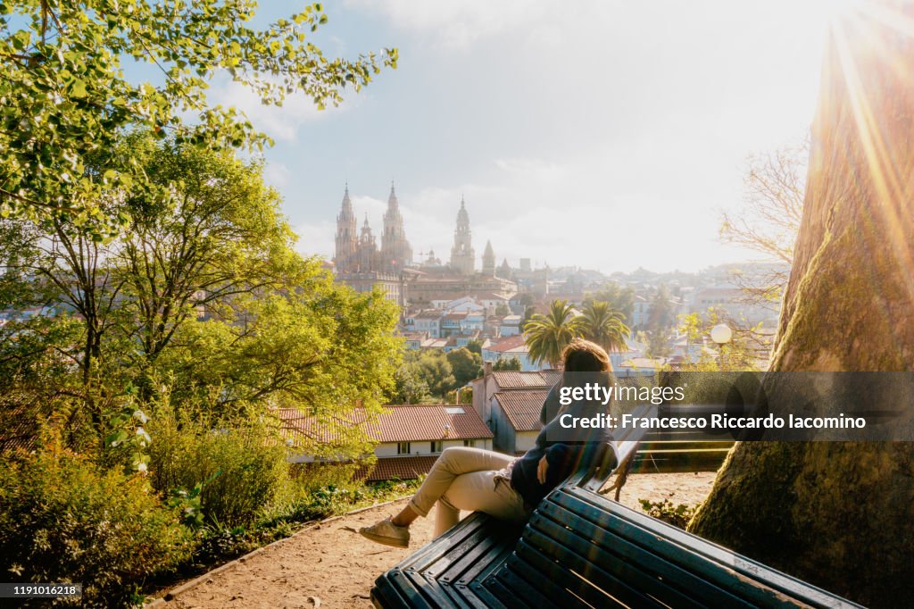 Woman watching Santiago de Compostela Cathedral at sunrise, park and sunny sky. Galicia, Spain