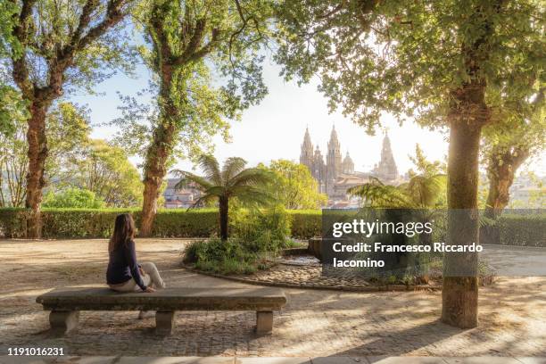 woman in a park bench watching santiago de compostela cathedral at sunrise, park and sunny sky. galicia, spain - santiago de compostela stockfoto's en -beelden