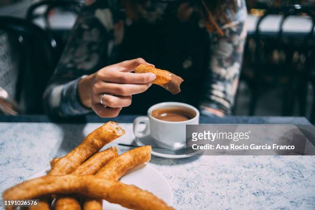 a girl dipping a churro in hot chocolate at a local coffee shop - churro stockfoto's en -beelden