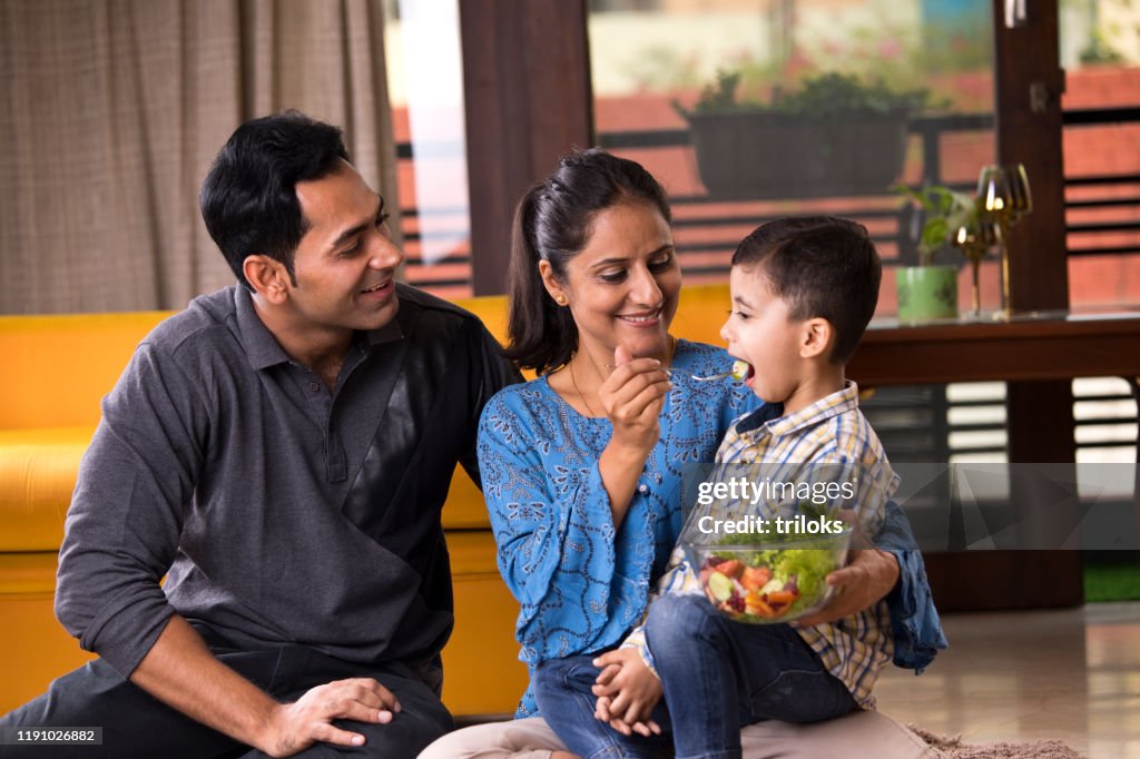 Happy woman feeding fruit salad to son