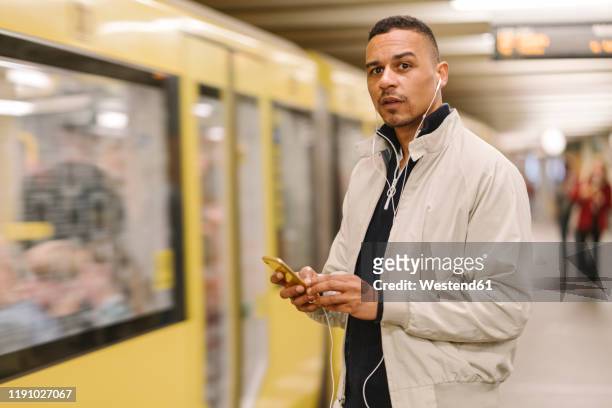 portrait of man at underground station platform using earphones and cell phone, berlin, germany - passant stock-fotos und bilder