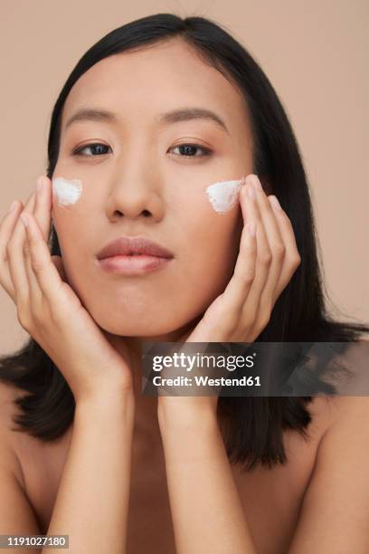 portrait of young female chinese woman applying cream - crema facial fotografías e imágenes de stock