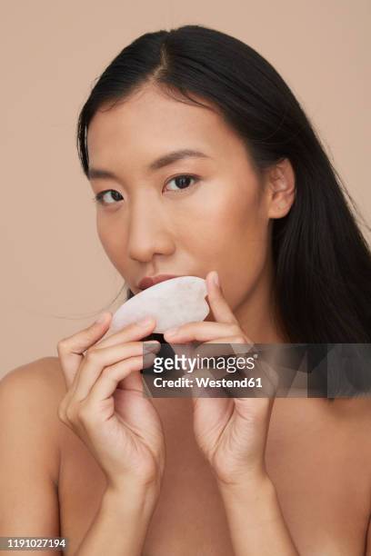 portrait of young female chinese woman using gua sha stone - spooning stock pictures, royalty-free photos & images