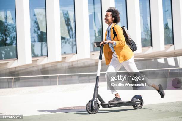 happy young woman with earphones riding e-scooter in the city - push scooter stock pictures, royalty-free photos & images