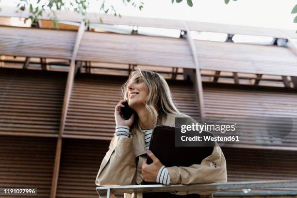 young blond woman using smartphone, holding laptop bag - laptoptasche stock-fotos und bilder