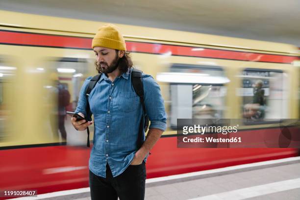 bearded man with backpack looking  at smartphone while waiting at platform, berlin, germany - nahverkehr stock-fotos und bilder
