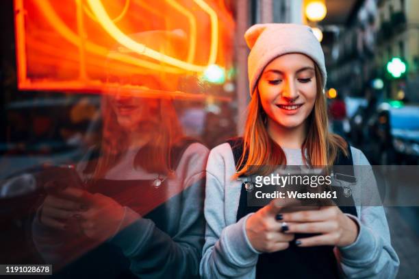 smiling young woman standing next to neon light using her smartphone at night - people chatting stock-fotos und bilder