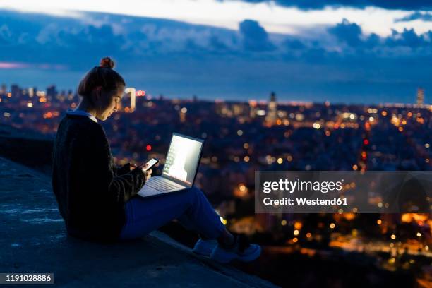 young woman using cell phone and laptop at dawn above the city, barcelona, spain - computer equipment stock pictures, royalty-free photos & images