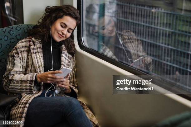 young woman with earphones using smartphone on a subway - tren de metro fotografías e imágenes de stock