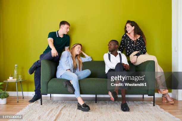 casual colleagues talking on a sofa in a green walled office lounge - four people stock pictures, royalty-free photos & images