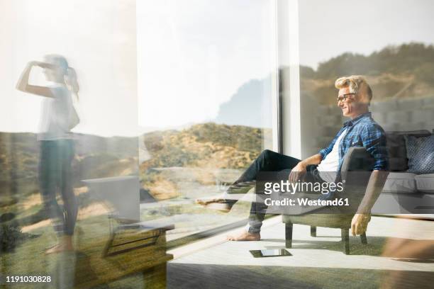 casual man sitting in modern home with woman standing in garden - mid adult stock-fotos und bilder