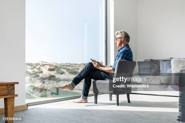 casual businessman sitting in modern home using tablet - glass business man stock-fotos und bilder