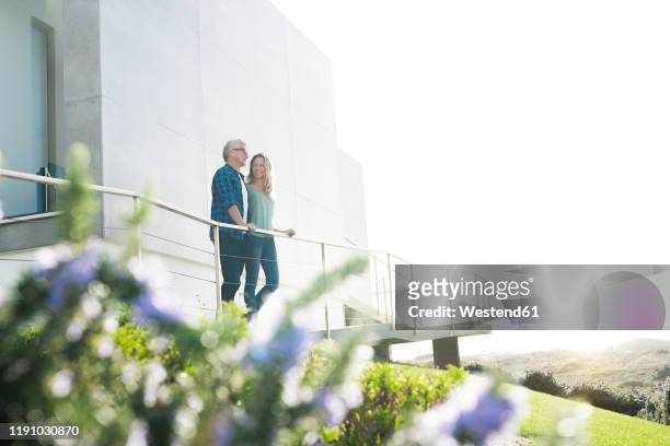 smiling couple standing in front of their modern home - luxury property stock-fotos und bilder