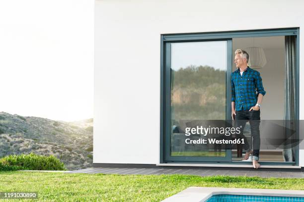 casual man standing in front of his modern home with pool looking at the landscape - looking outside window stock-fotos und bilder