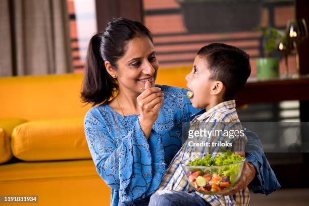 happy mother feeding fruit salad to son - healthy eating stock pictures, royalty-free photos & images