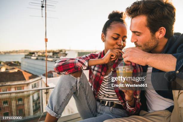 young couple sharing a drink on rooftop in the evening - cocktail sonnenuntergang stock-fotos und bilder