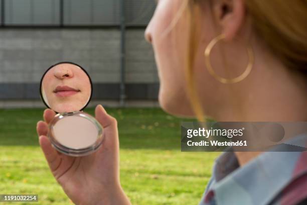 young woman with nose piercing looking at beauty mirror in her hand - nose piercing - fotografias e filmes do acervo