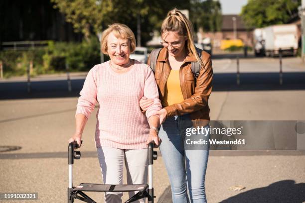 granddaughter assisting her grandmother walking with wheeled walker - oma rollator stockfoto's en -beelden