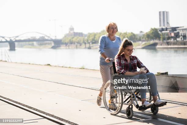 grandmother with her granddaughter sitting in wheelchair - rollstuhl schieben stock-fotos und bilder