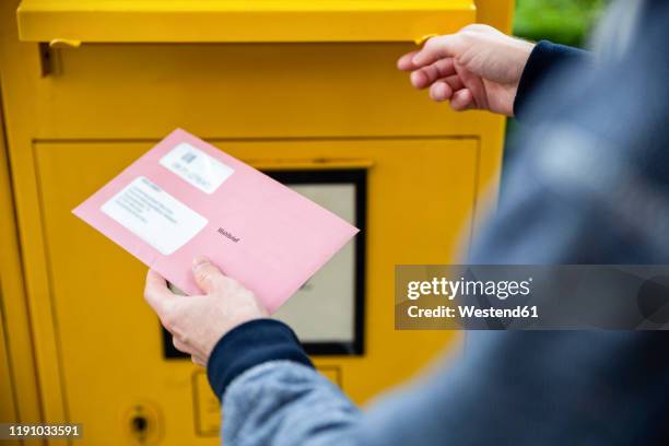 elector holding documtents for the postal vote in front of the mailbox - abschicken stock-fotos und bilder