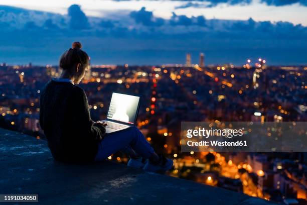 young woman using laptop at dawn above the city, barcelona, spain - grand lit stock pictures, royalty-free photos & images