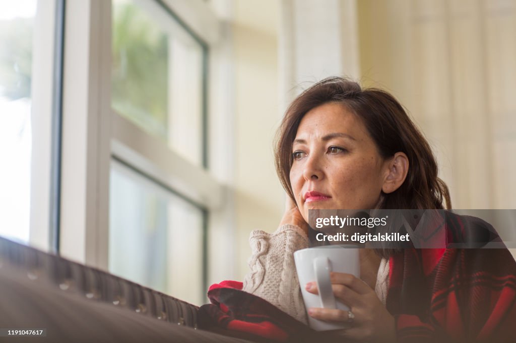 Mujer madura mirando por la ventana sintiéndose triste.