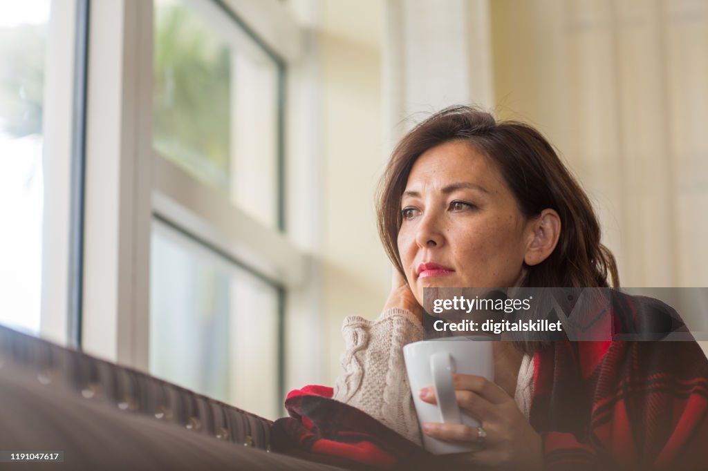 Mature woman looking out the window feeling sad.