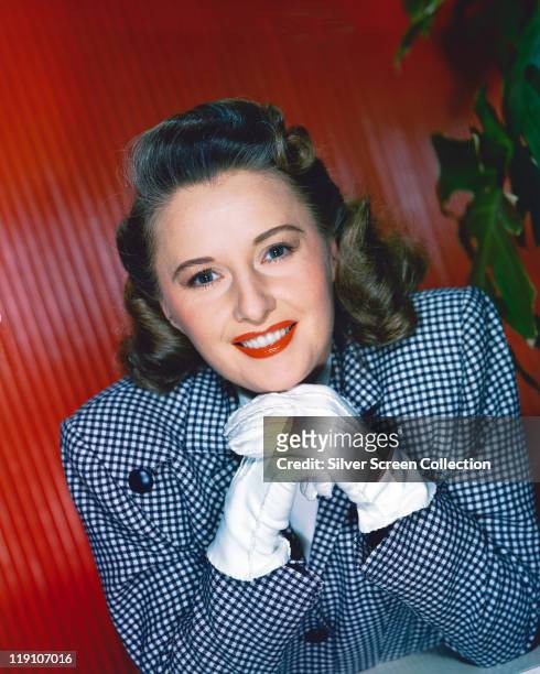 Barbara Stanwyck , US actress, wearing a blue-and-white jacket and resting her chin on her hands in front of her, wearing white gloves, circa 1940.