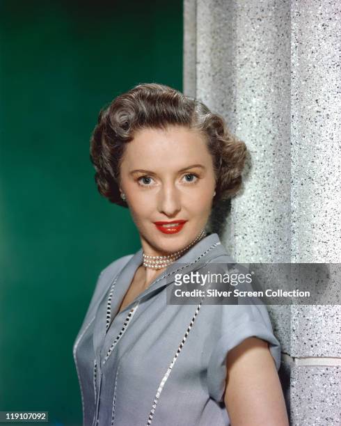 Barbara Stanwyck , US actress, poses in a studio portrait, against a green background, circa 1950.