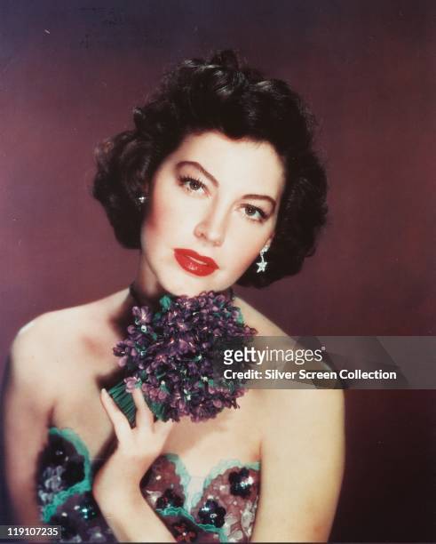 Ava Gardner , US actress, wearing a purple-and-green shoulderless dress, and holding a purple-and-green corsage, in a studio portrait, circa 1955.