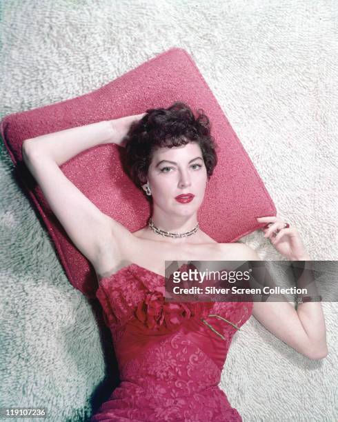Ava Gardner , US actress, reclining with her head on a red pillow, wearing a red shoulderless dress, in a studio portrait, circa 1960.