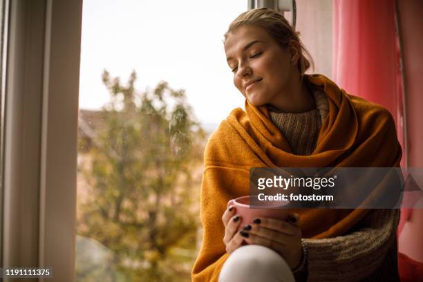smiling young woman enjoying a warm cup of tea on a cold autumn day - cosy stock pictures, royalty-free photos & images