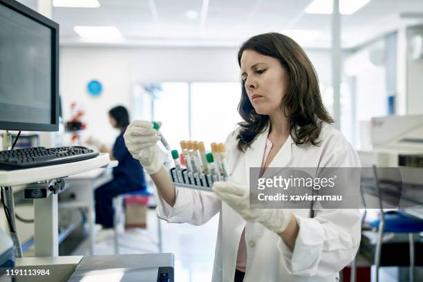 pathologiste femelle mûre examinant des échantillons de tube d'essai dans le laboratoire - pathologist photos et images de collection