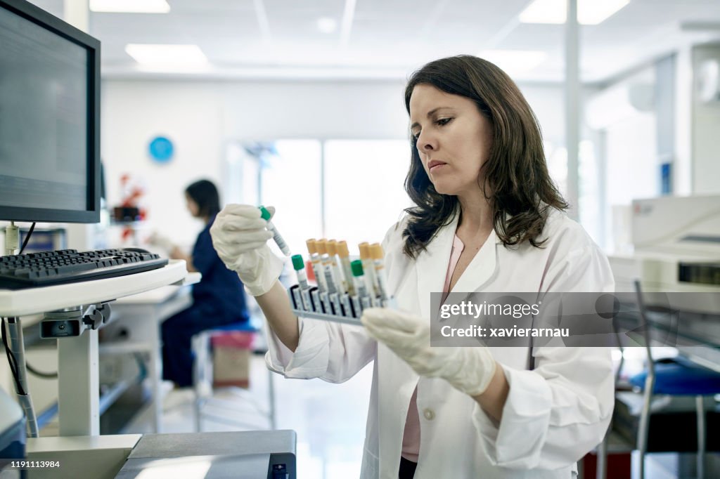 Mature Female Pathologist Examining Test Tube Samples in Lab